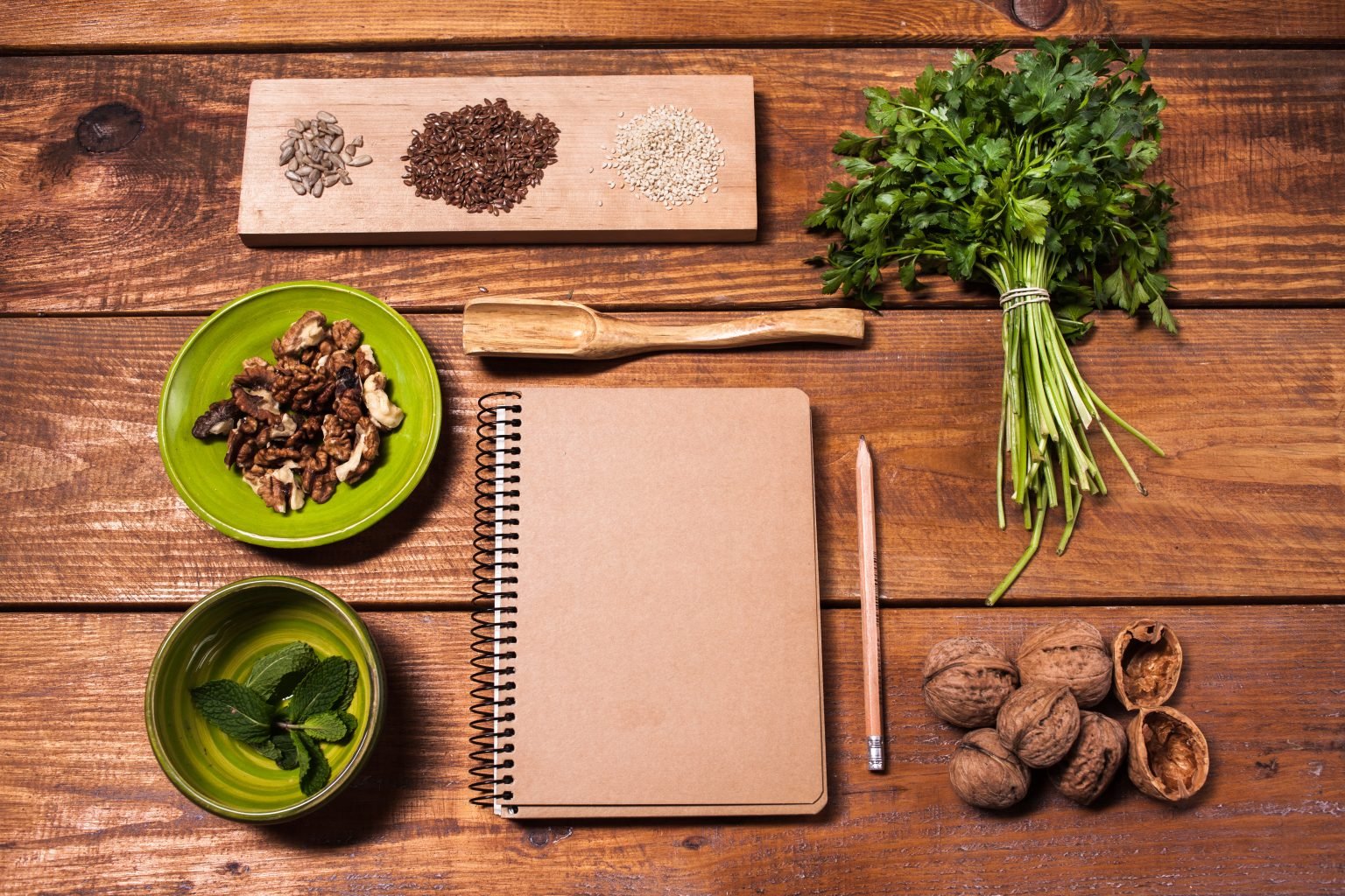 Notebook for recipes, pencil, walnuts, parsley and seeds on wooden table.